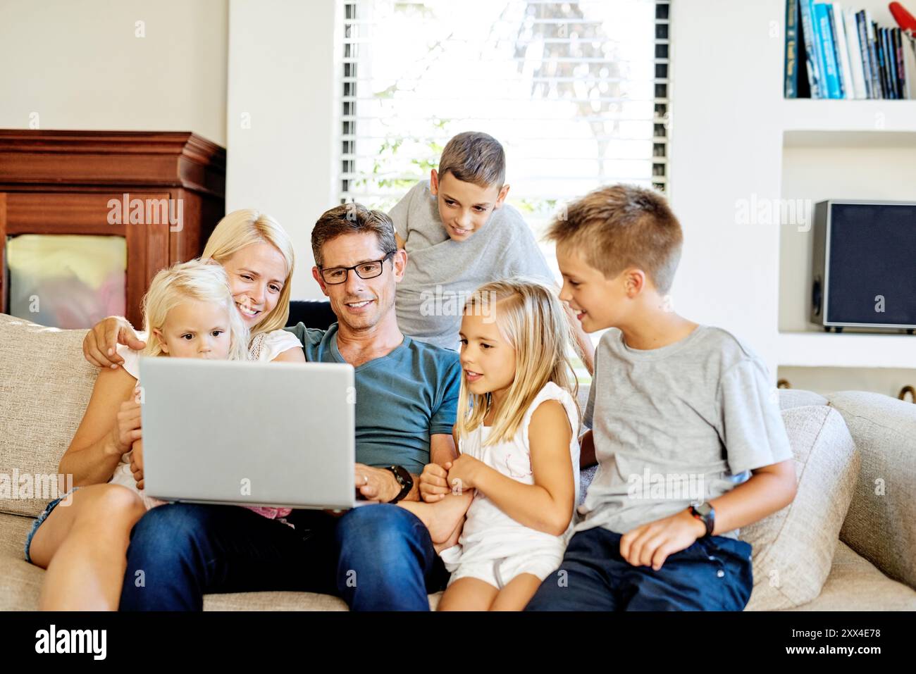 Mutter, Vater und Kinder auf Sofa mit Laptop, Online-Cartoon und Abonnement mit Verbindung. Familienheim, Mutter und Vater mit Kindern zum Streaming Stockfoto