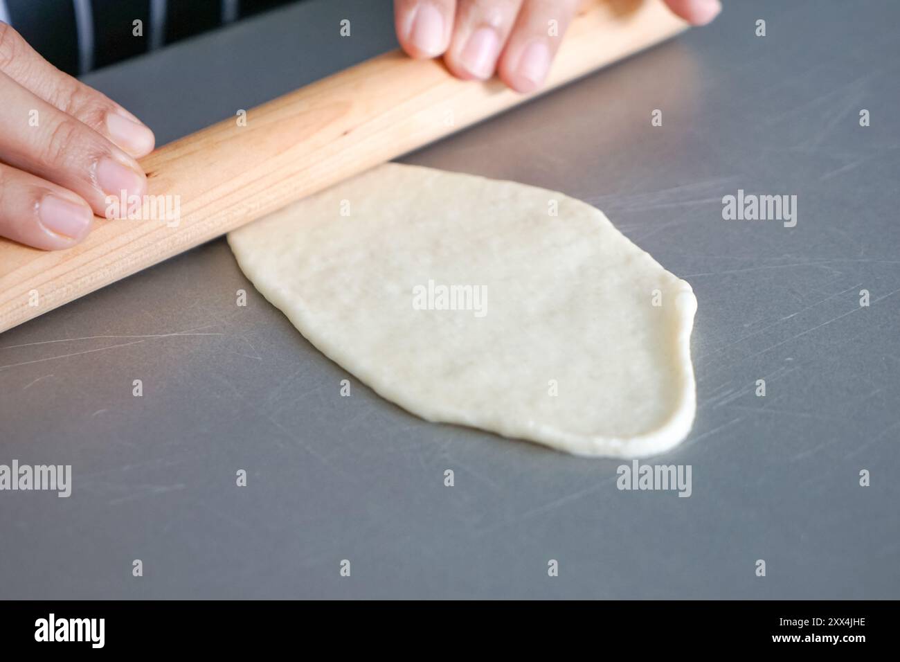 Teig mit einer Holzrolle handrollen. Stockfoto