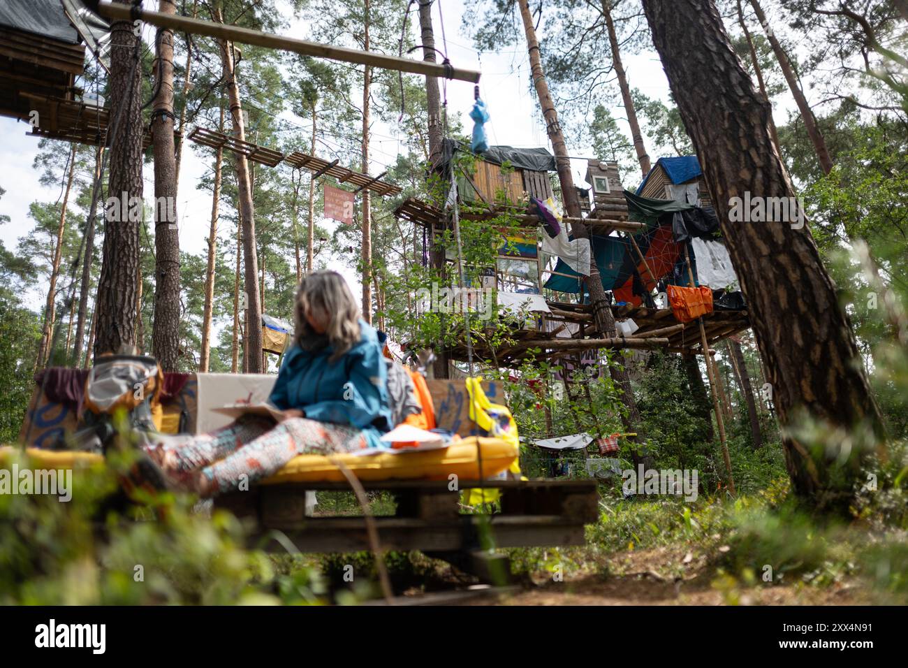22. August 2024, Brandenburg, Grünheide: Ein Besucher sitzt im Protestlager der Tesla-Fabrik, die von der Initiative "Stop Tesla" betrieben wird. Seit Ende Februar besetzen die Aktivisten einen Waldabschnitt neben der Fabrik des Elektroautos. Foto: Sebastian Gollnow/dpa Stockfoto
