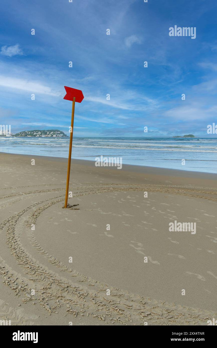 Ein rotes Schild im Sand am Strand weist auf eine gefährliche Zone im Meer hin, sodass Schwimmer diesen Bereich nicht betreten. Der Enseada Beach in Guaruja Stockfoto