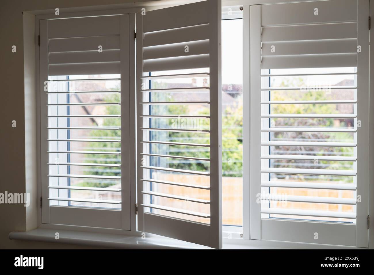 Drei Rahmen aus weißen, modernen Holzläden über einem Fenster. Ein Abschnitt ist geöffnet. Die Verschlussleisten werden in verschiedene Positionen geschwenkt. Stockfoto