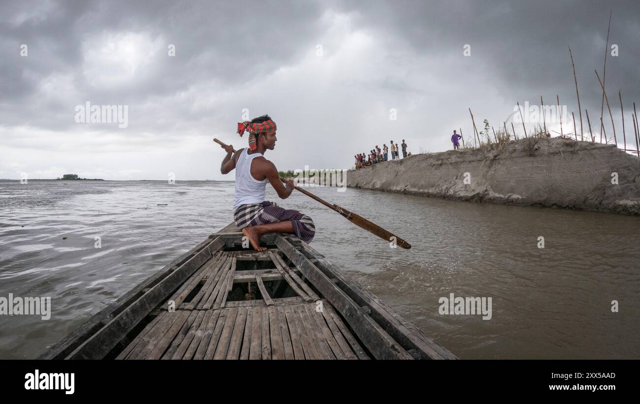 Rashed paddelt mit seinem Landboot an der Seite der Dorfbewohner auf der Kheyar Alga char am Brahmaputra River. Die letzte Rekordflut überschwemmte den Saibling und spülte all ihre Ernte und viele ihrer Häuser weg. Das Wasser ist inzwischen zurückgegangen, aber die Ernten sind verschwunden, ebenso wie große Teile ihres Landes. Stockfoto