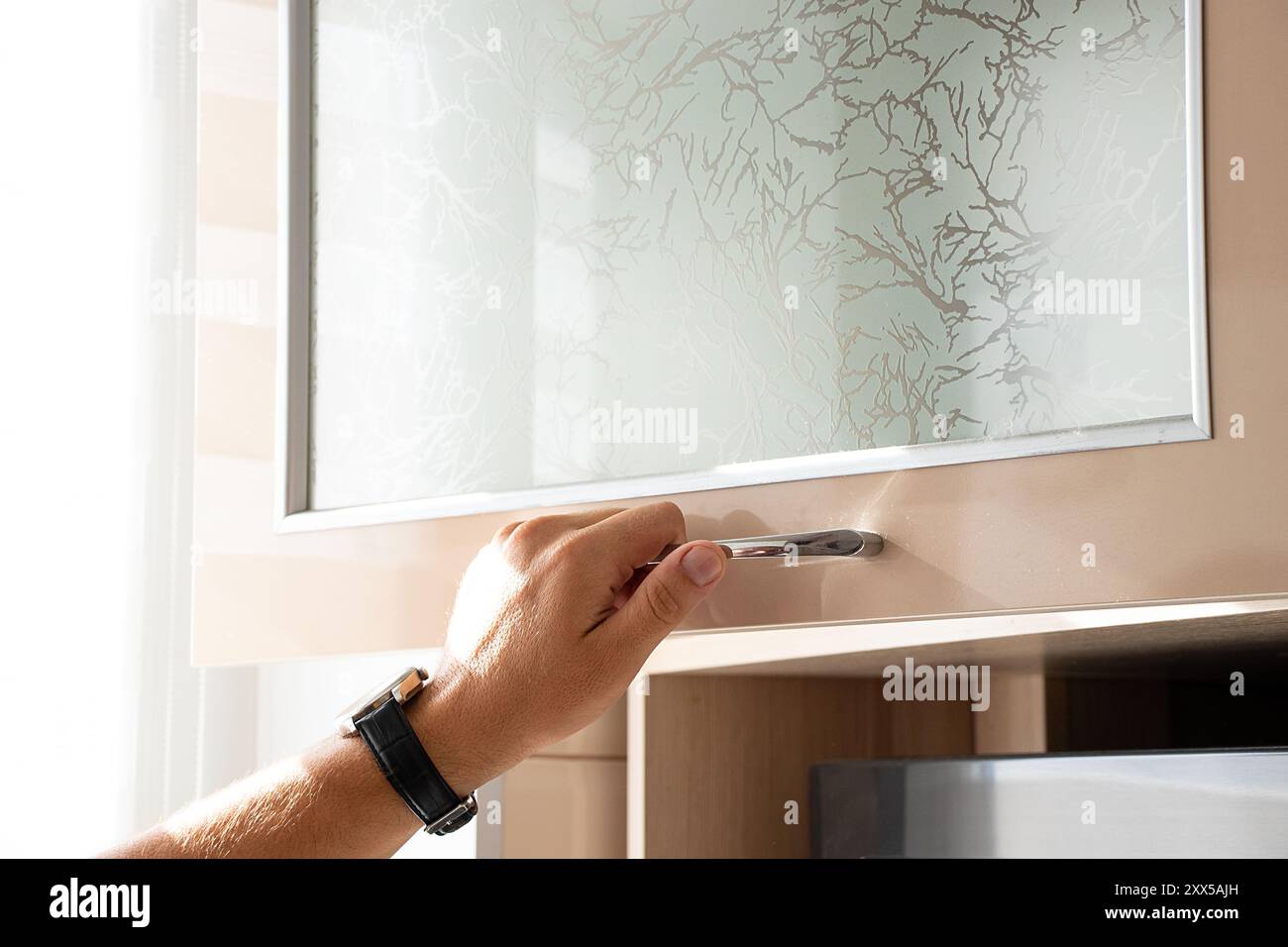 Männliche Hand öffnet beige Küchenschrank in der Küche in der Wohnung, Küchenmöbel Stockfoto