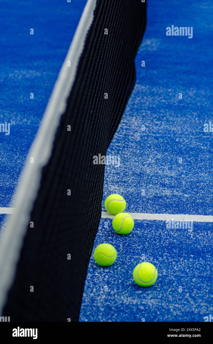 Vier Paddle-Tennisbälle neben dem Netz eines blauen Paddle-Tennisplatzes, Racketsportkonzept Stockfoto
