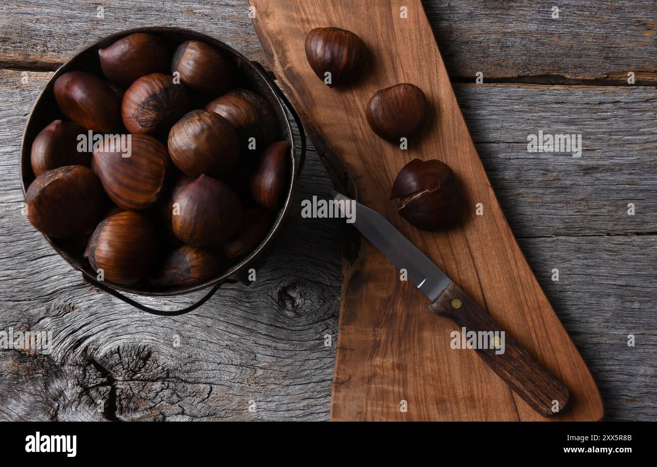 Ein Eimer frischer Kastanien und ein Messer auf einem Schneidebrett. Stockfoto