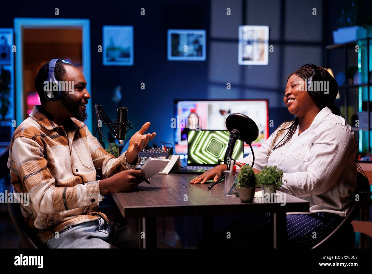 Podcaster, die im Heimstudio fröhliche Gespräche mit Online-Zuhörern genießen und ein breites Themenspektrum abdecken. Ein Mann, der ein Notebook trägt, spricht mit Sozialisten und sie haben eine gute Diskussion. Stockfoto