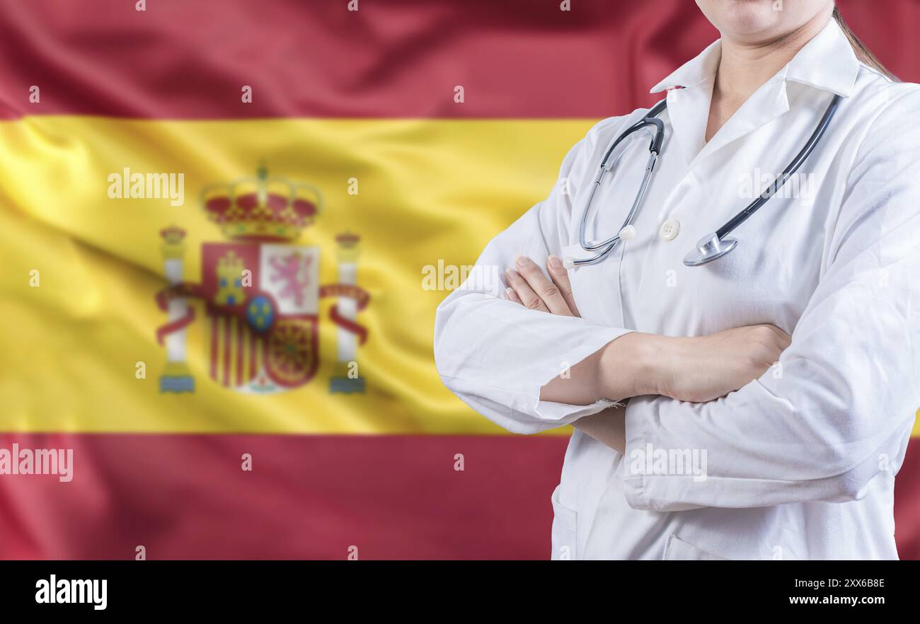 Ärztin mit Stethoskop auf Spanienflagge. Spanisches Gesundheits- und Pflegekonzept. Doktor mit gekreuzten Armen auf spanischer Flagge Stockfoto