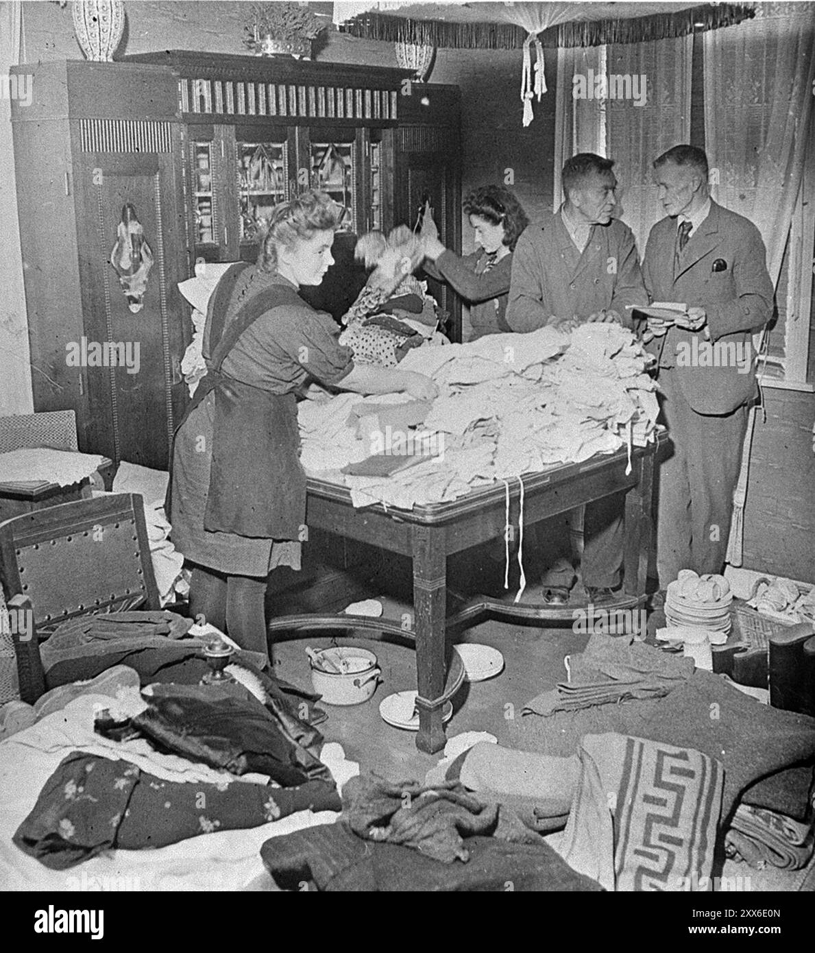 Ilse Kohra(L), Tochter des Burgermeisters der deutschen Stadt Belsen, sortierte zusammen mit Herrn Pfeifer(R) und seiner Tochter Anna im Haus des Burgermeisters Kleidung für die Überlebenden Bergen-Belsens. Stockfoto