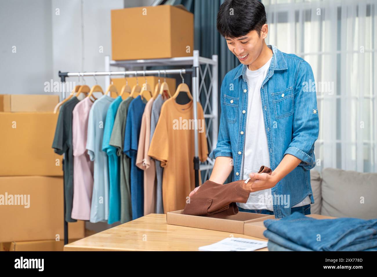 Junger Online-Verkäufer, der sein Hemdprodukt in die Verpackung packt, um es von seinem Heimstudio an seinen Kunden zu versenden Stockfoto