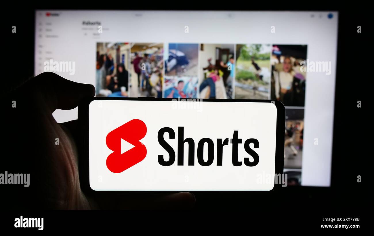 Person, die ein Mobiltelefon mit dem Logo des kurzen Video-Sharing-Dienstes YouTube Shorts vor der Unternehmenswebseite hält. Schwerpunkt auf dem Display des Telefons. Stockfoto