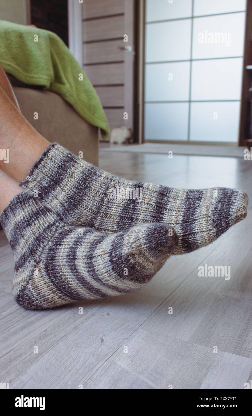 Herrenbeine in gestrickten gestreiften Socken. Stricksocken aus Wolle an überkreuzten Beinen. Warme Herbstkleidung. Gestreiftes Häkelmuster für Socken. Handgemachte Mode. Stockfoto