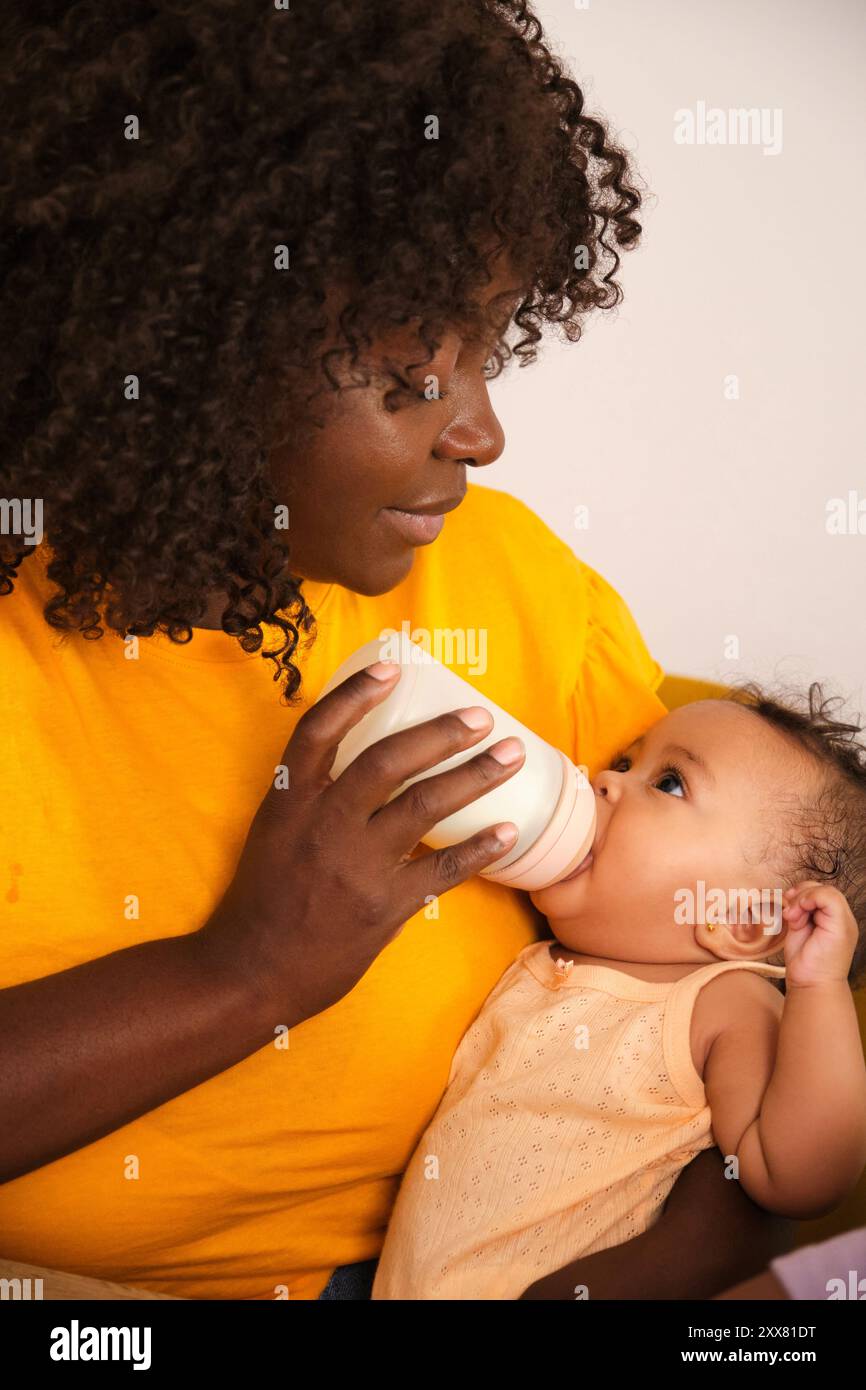 Liebevolle Mutterflasche, die ihr Mädchen auf weißem Hintergrund füttert Stockfoto