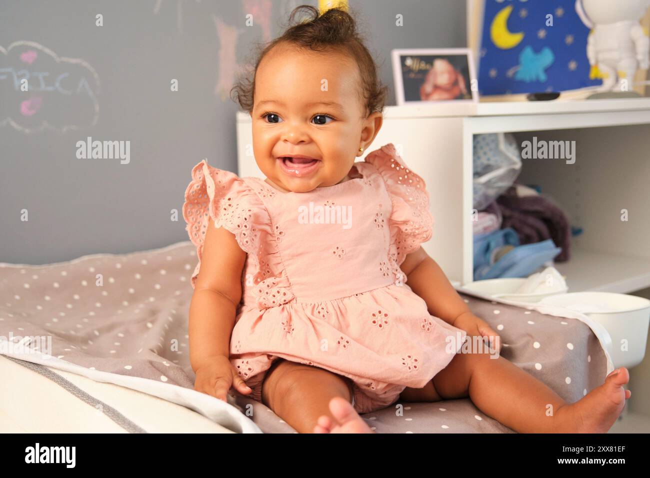 Entzückendes Mädchen lächelt und sitzt auf Wickelauflage im Kinderzimmer Stockfoto