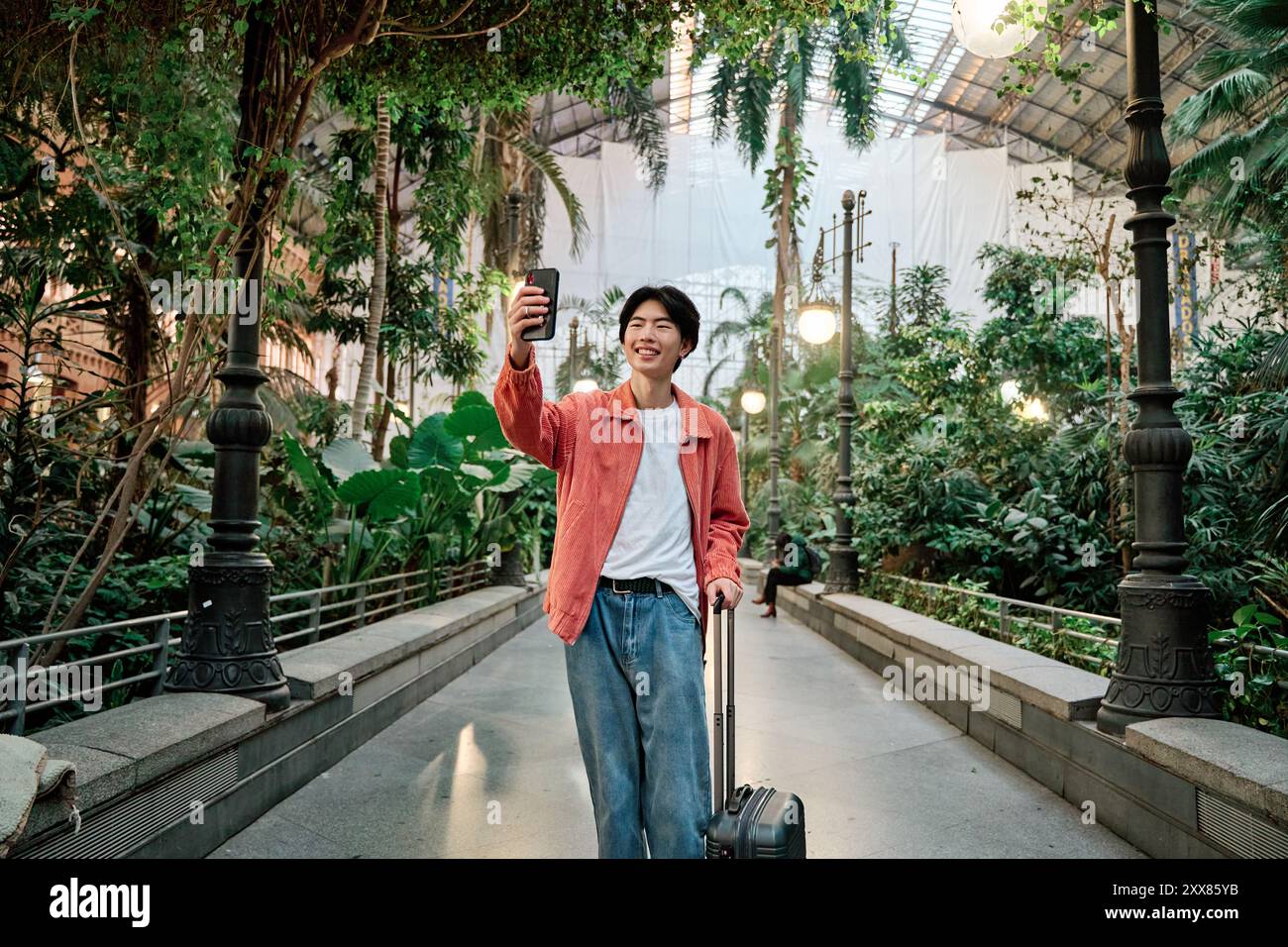 Porträt eines asiatischen Mannes, der mit einem Koffer am Bahnhof einen Videoanruf macht Stockfoto