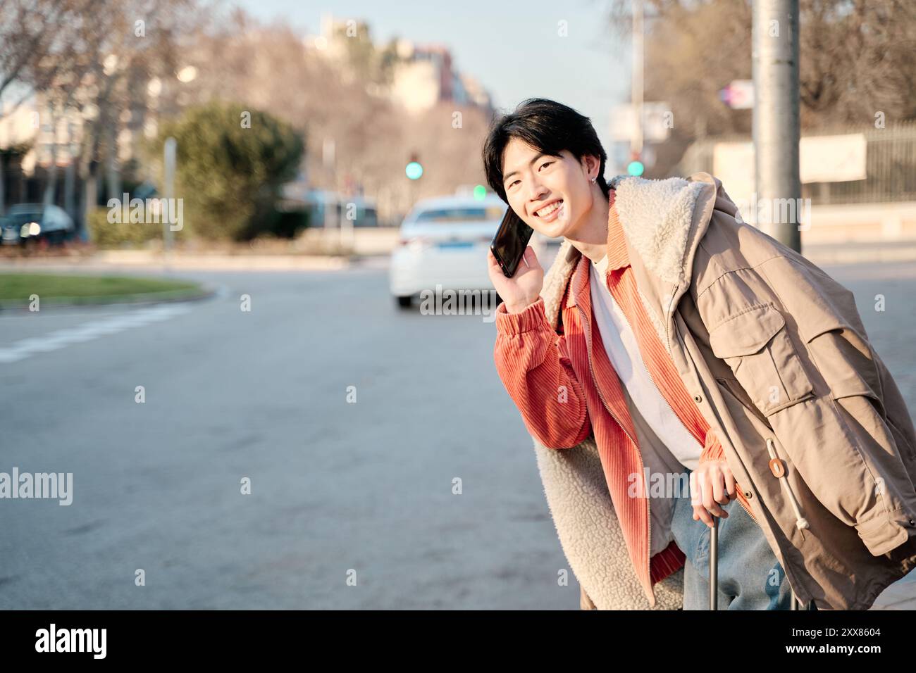 Stilvoller junger asiatischer Mann stilvoller junger asiatischer Mann, der am Telefon spricht und auf ein Taxi wartet, um auf eine Reise zu gehen Stockfoto