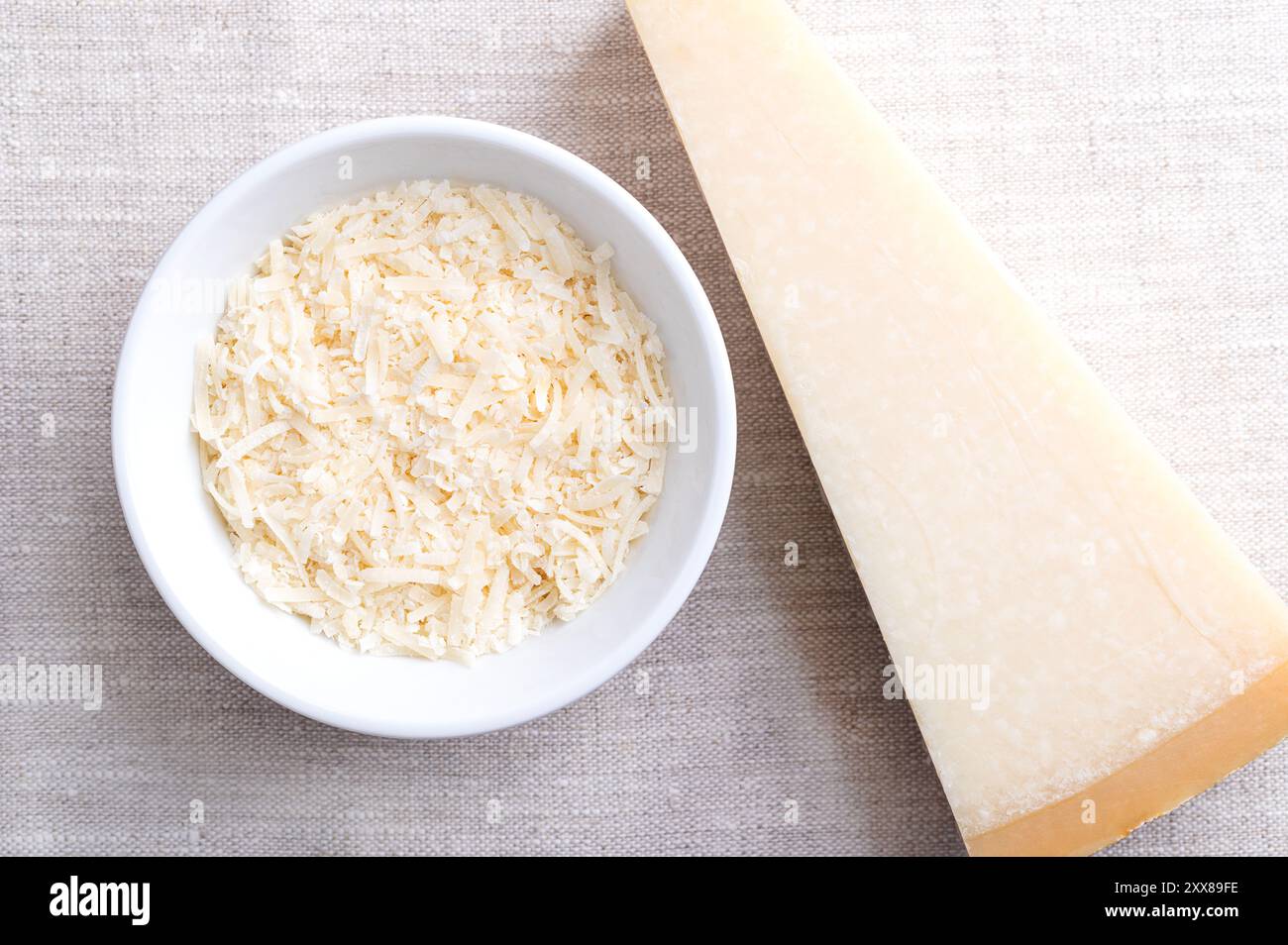 Geriebener Parmesankäse, Parmigiano Reggiano in einer Holzschale auf Leinen, mit einem ganzen Stück Käse auf der rechten Seite. Italienischer Hartkäse mit Granulat. Stockfoto