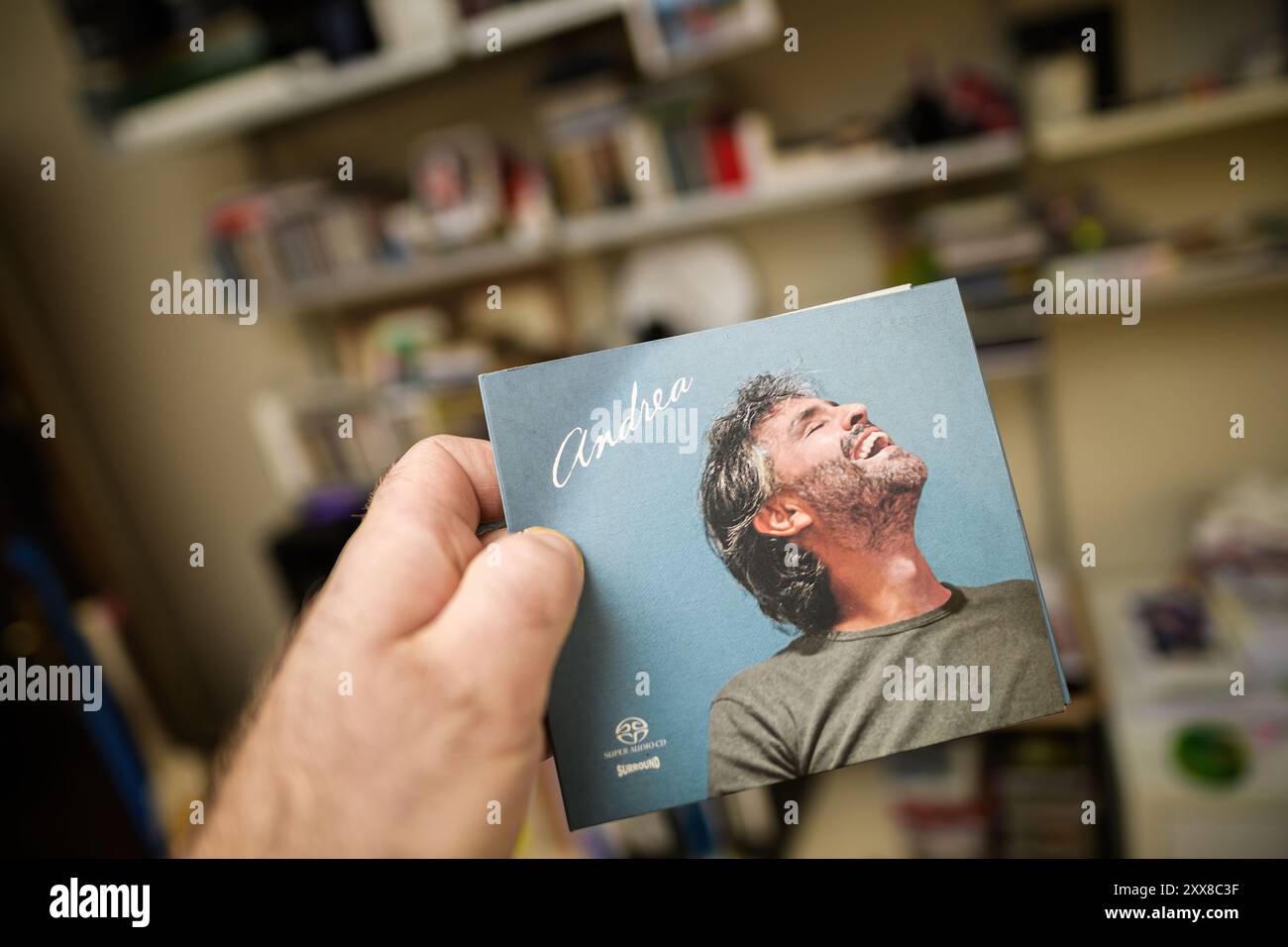 Paris, Frankreich - 29. Februar 2024: Eine männliche Hand hält eine Andrea Bocelli SACD mit Hüllen vor dem Hintergrund von Musikplatten, die den Fokus auf den Künstler und die musikalische Sammlung hebt Stockfoto