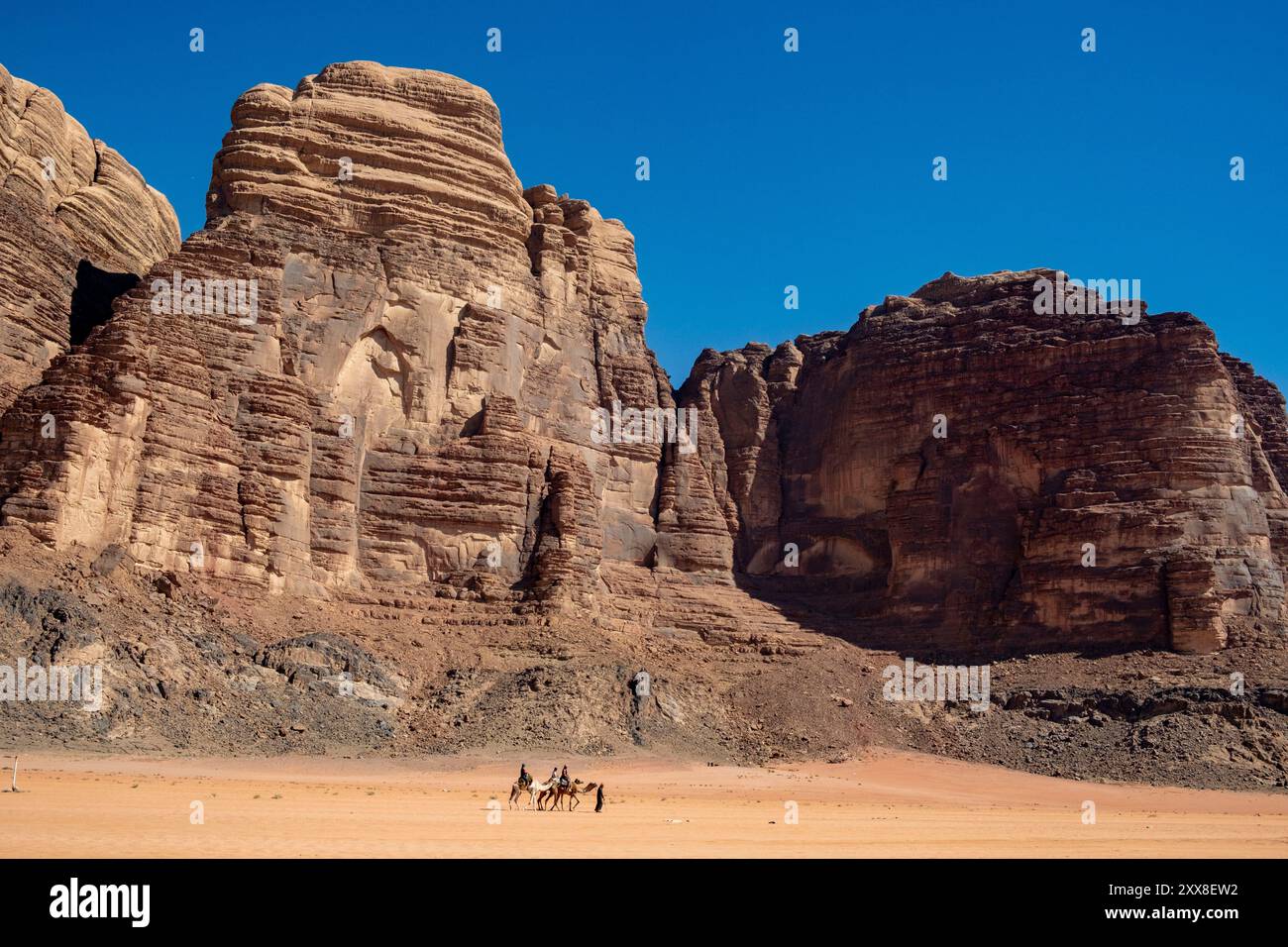 Jordanien, die Wüste Wadi Rum, die von der UNESCO zum Weltkulturerbe erklärt wurde, Touristen auf Kamelen mit ihrem Beduinenführer vor den Sandsteinklippen Stockfoto