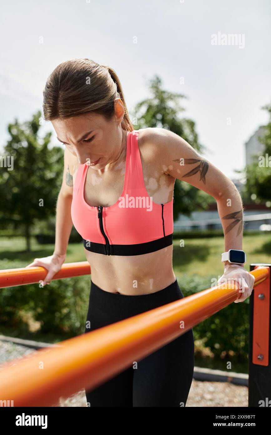Eine junge Frau in rosa Oberteil und schwarzer Leggings taucht in einer Bar im Park und zeigt Stärke und Entschlossenheit Stockfoto