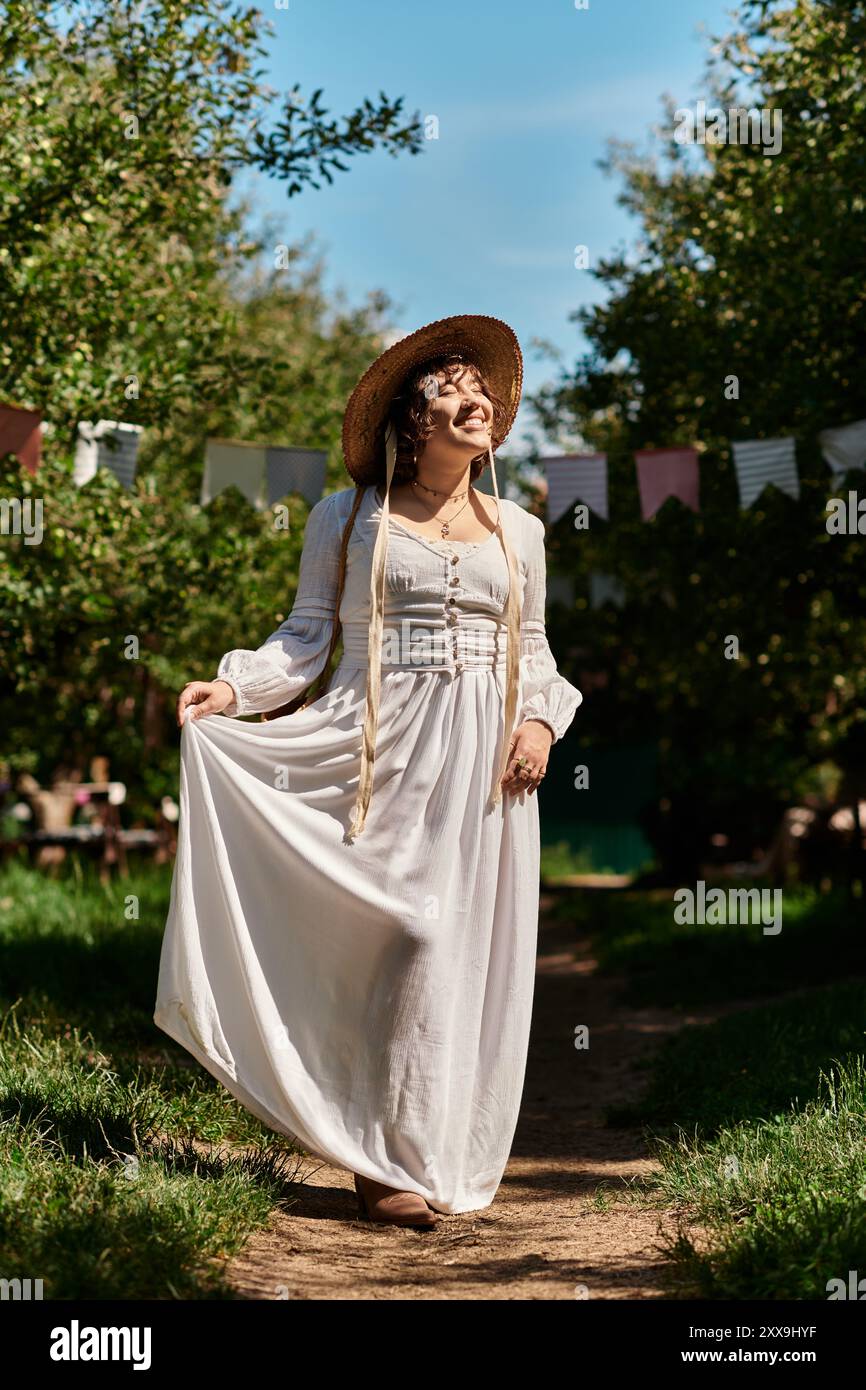 Eine junge Frau in weißem Kleid und Strohhut geht auf einem Weg in einem Garten entlang, umgeben von grünen Bäumen und blauem Himmel. Stockfoto