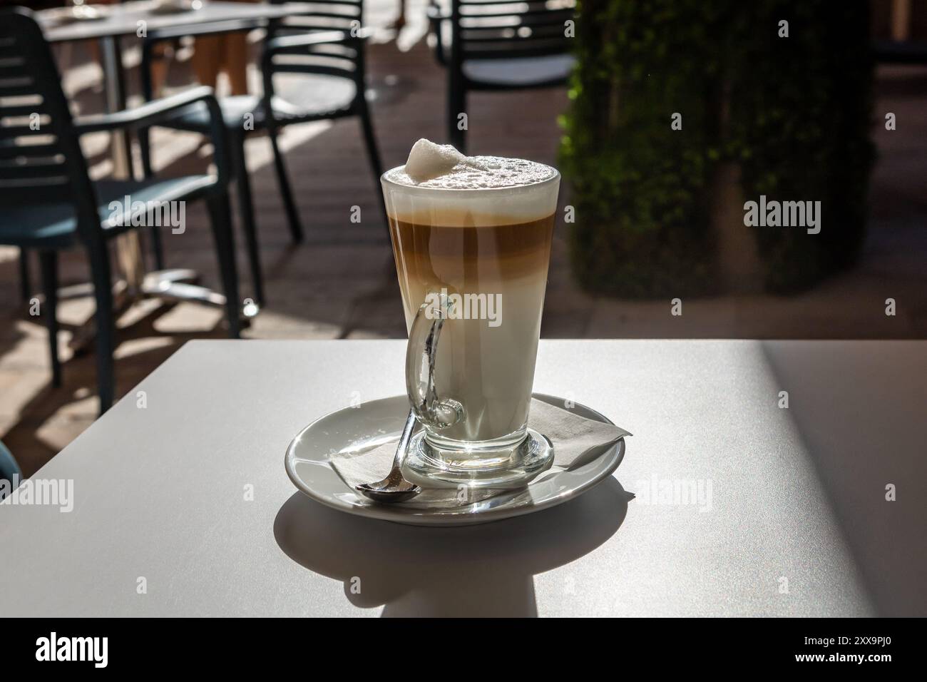 Mehrschichtiger Kaffee-Latte in einem hohen Glas auf dem Tisch in einem Café auf der Straße. Verschwommener Hintergrund, keine Leute. Stockfoto