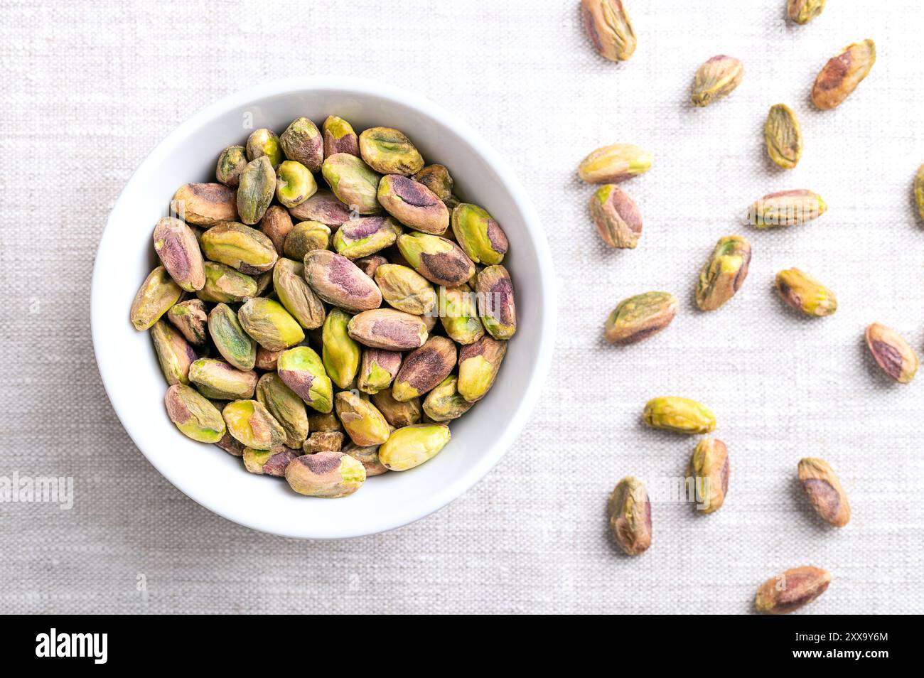 Pistazien-Kerne, geröstete und gesalzene Nüsse in einer weißen Schüssel auf Leinengewebe. Geschälte Früchte von Pistacia Vera, knusprig geröstet und gesalzen. Stockfoto