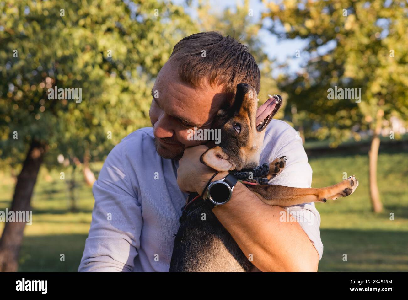 Ein lächelnder Mann mittleren Alters spaziert und spielt mit einem kleinen Hund im öffentlichen Park Stockfoto