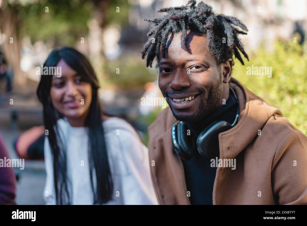 Porträt eines fröhlichen afrikanischen Mannes mit Dreadlocks, die Kopfhörer tragen, begleitet von einer lächelnden Frau mit langen dunklen Haaren. Vielseitiges Paar genießt urb Stockfoto