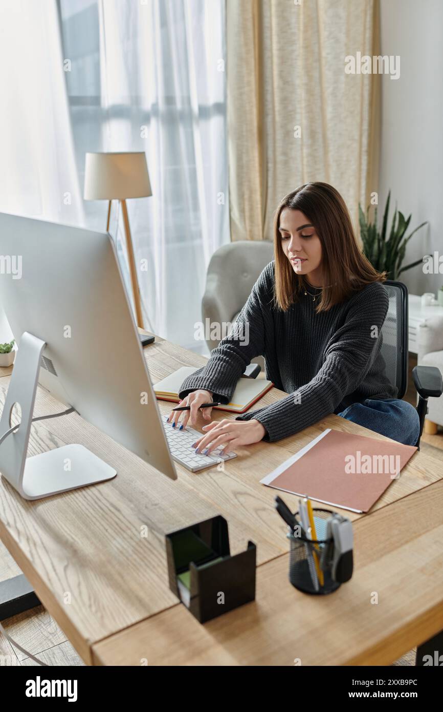Eine junge Frau sitzt an einem Schreibtisch und tippt auf einer Computertastatur, während sie von zu Hause aus arbeitet. Stockfoto