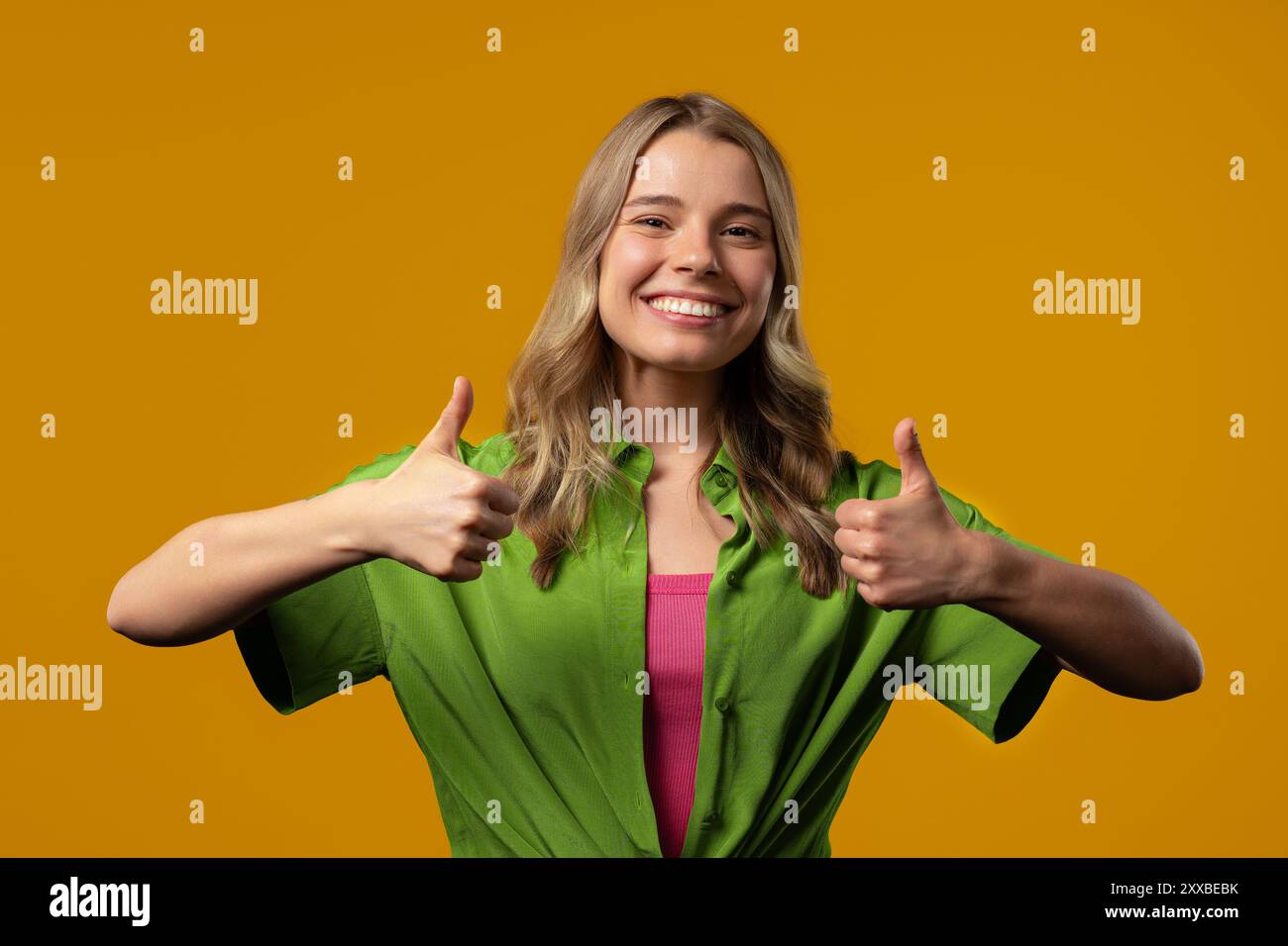 Stilvolle Frau mit Handzeichen, Daumen-hoch-Geste. Glückliche Dame, richtige perfekte Wahl, tolles Angebot, gelber Hintergrund. Positives weibliches Model lächelt Stockfoto