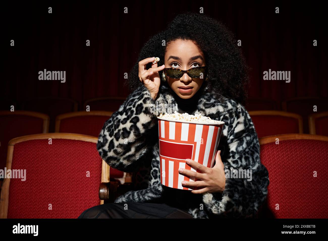 Stilvolle Frau in einem Kino, Popcorn hält und einen Film ansieht. Stockfoto