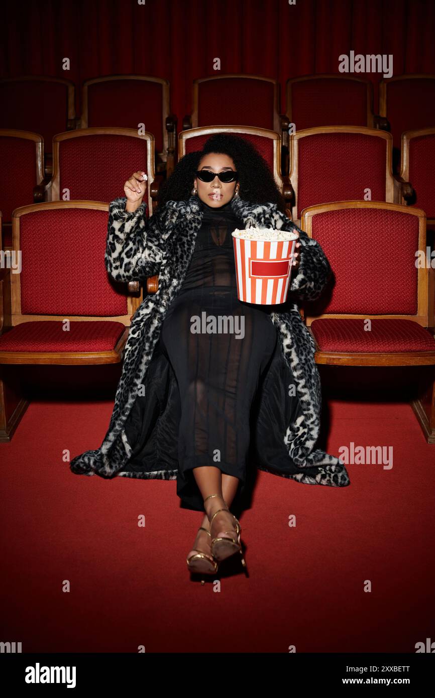 Eine modische Frau im Leopardenmantel genießt einen Film mit Popcorn in der Hand. Stockfoto