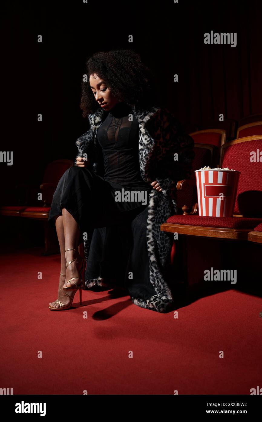 Eine stilvolle Frau in einem Mantel mit Leopardenmuster sitzt in einem dunklen Kino, vertieft in den Film, der auf dem Bildschirm spielt. Stockfoto
