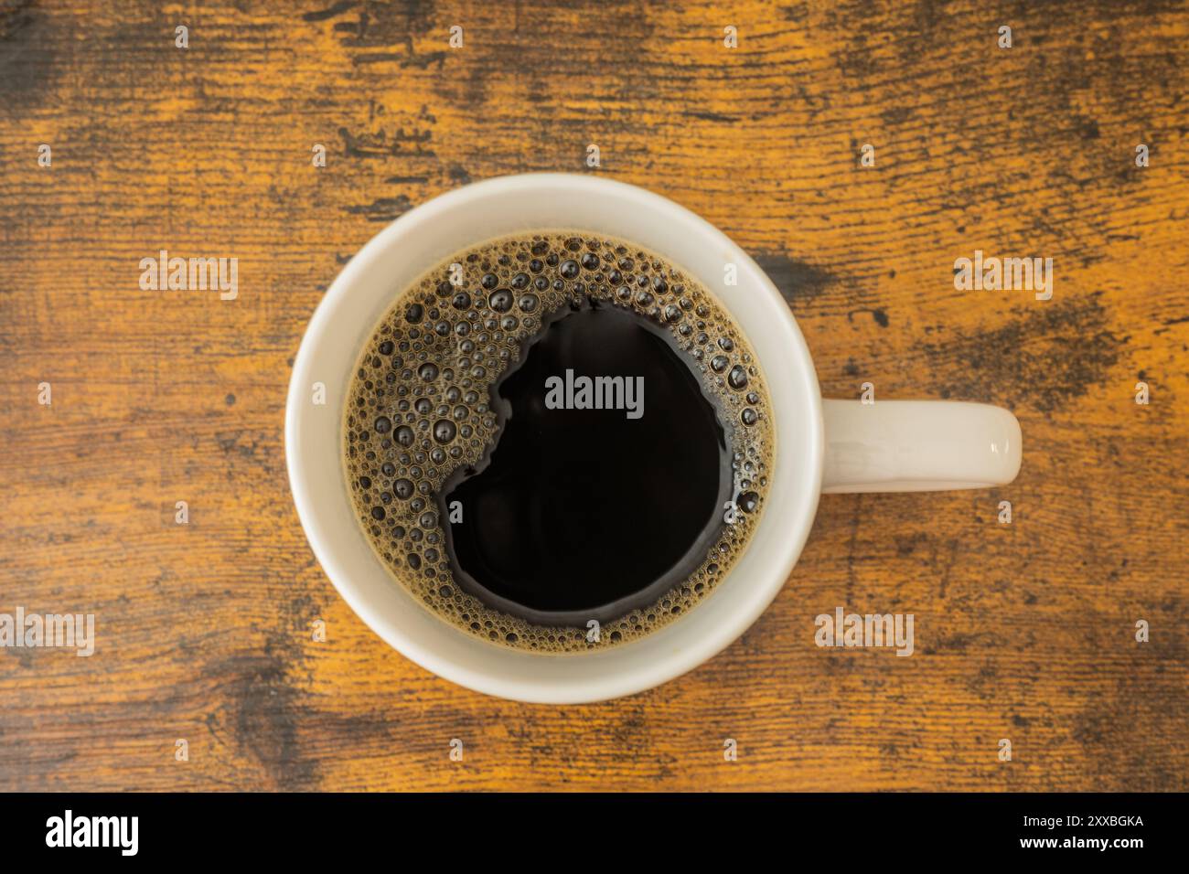 Kaffeeholz Hintergrund weiße Tasse von oben. Kaffee brauner Holzhintergrund mit sichtbaren Holzkörnern und Blasen vom Kaffee sichtbar in weißen Becheroberflächen Stockfoto