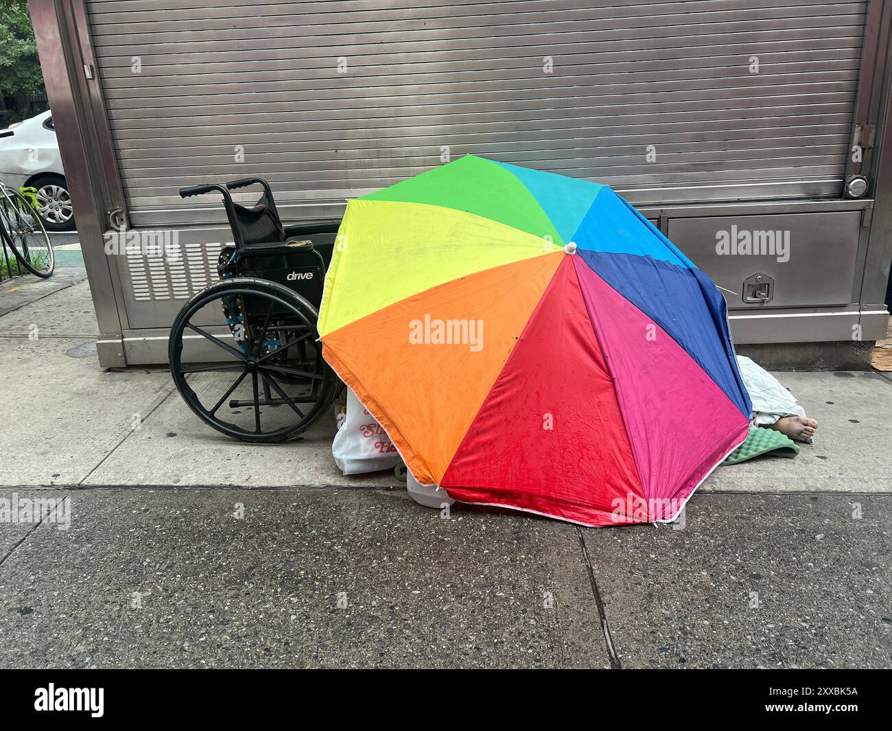 Behinderte Obdachlose schläft an einem heißen Sommertag in Manhattan, New York City, im Schatten eines Sonnenschirms. Stockfoto