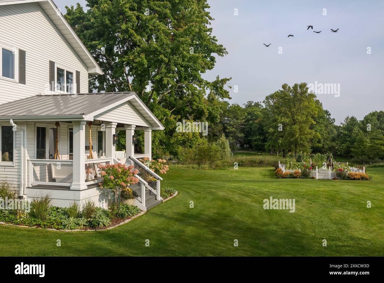 Vor dem weißen Bauernhaus mit großem grünen Vorgarten und hübschem umzäuntem Garten Stockfoto