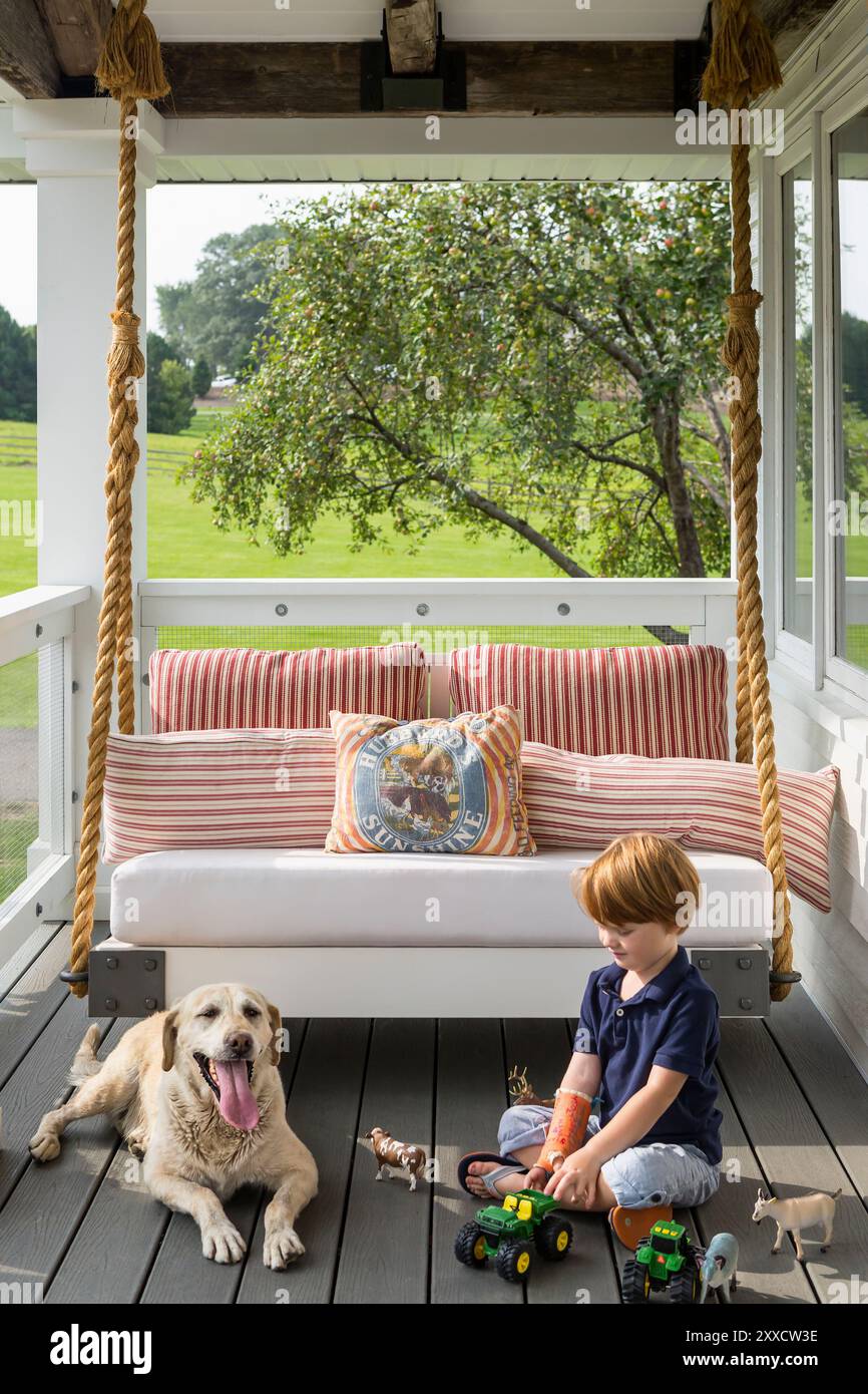 Ein kleiner Junge spielt mit Spielzeug auf der süßen Veranda neben seinem Hund Stockfoto