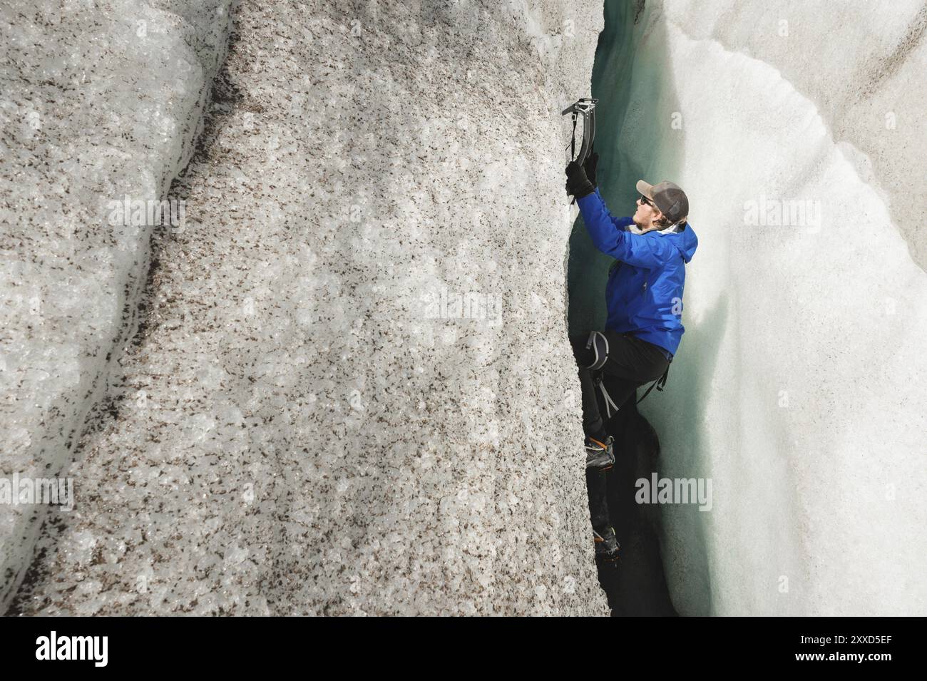 Ein freier Kletterer ohne Versicherung mit zwei Eisachsen steigt aus einem Riss im Gletscher auf. Freies Klettern ohne Seile Stockfoto