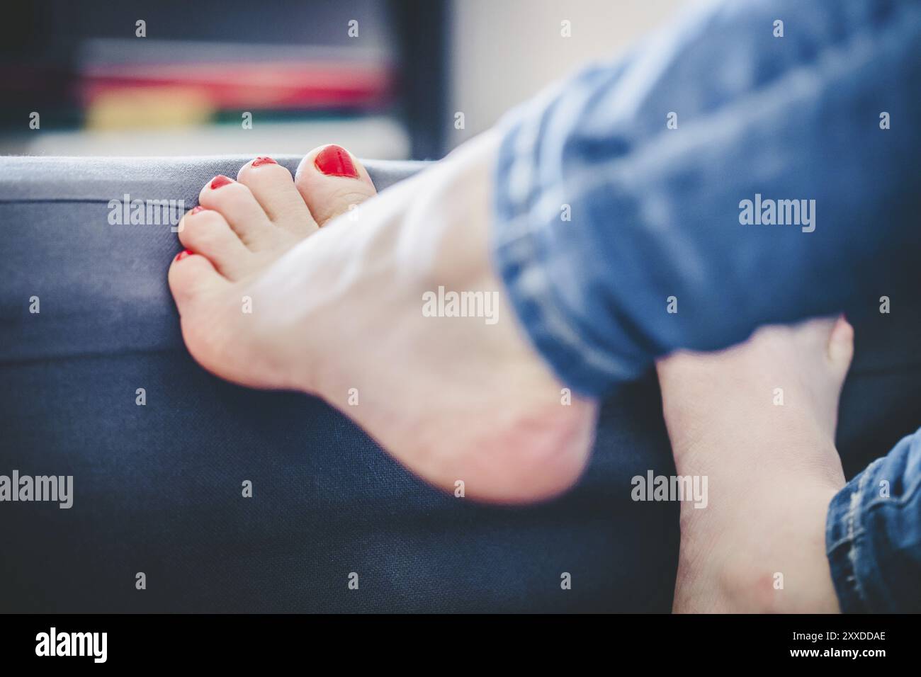 Nahaufnahme der weiblichen Füße mit rotem nagellack auf einer blauen Couch Stockfoto