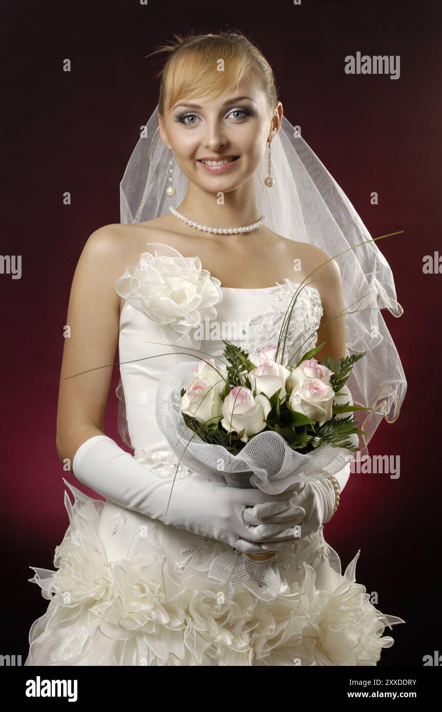 Junge schöne Braut in einem Hochzeitskleid mit einem Haufen weißer Rosen auf dunkelrot Stockfoto