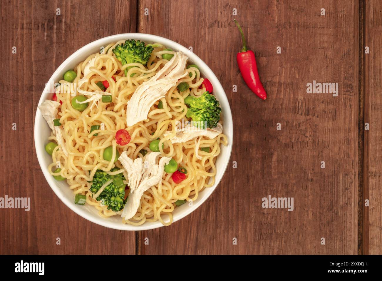 Nudeln mit Huhn, grünen Erbsen und Brokkoli, mit einem roten, heißen Chili-Pfeffer, von oben auf einem dunklen rustikalen hölzernen Hintergrund mit einem Platz für Tex Stockfoto