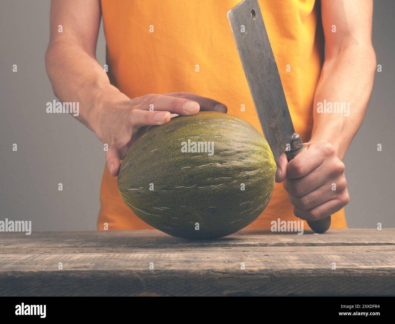 Junger Mann mit einem alten Cleaver und eine frische Melone auf eine rustikale Küche Tabelle Stockfoto