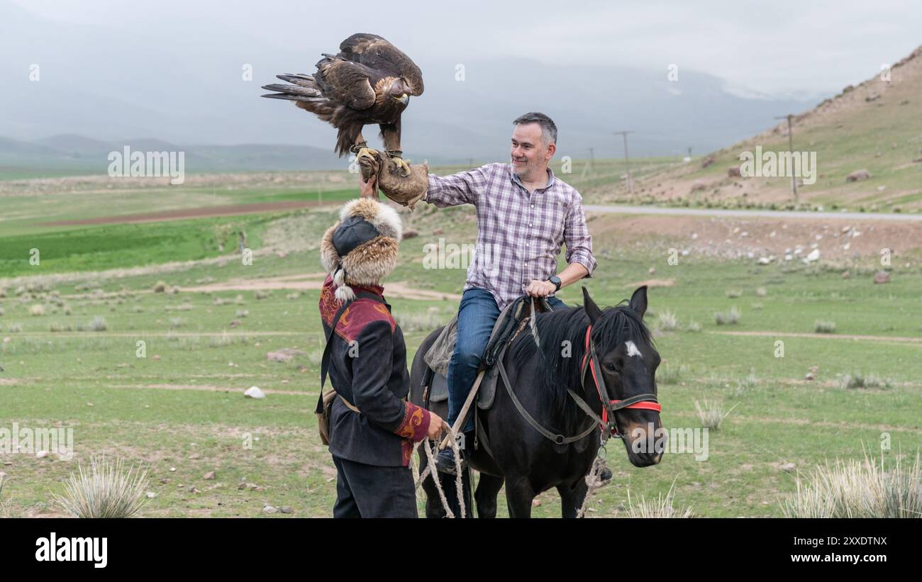 Issyk Kul, Kirgisistan - 23. Mai 2022: Adlertrainer hilft einem Touristen, einen goldenen Adler zu halten, ein Erlebnis-Urlaub Stockfoto