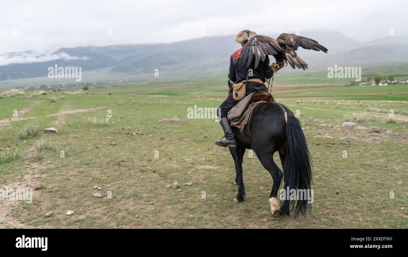 Issyk Kul, Kirgisistan - 23. Mai 2022: Adlertrainer zu Pferd mit seinem goldenen Adler, der traditionelle Jagdtechniken zeigt, die durch g übertragen wurden Stockfoto