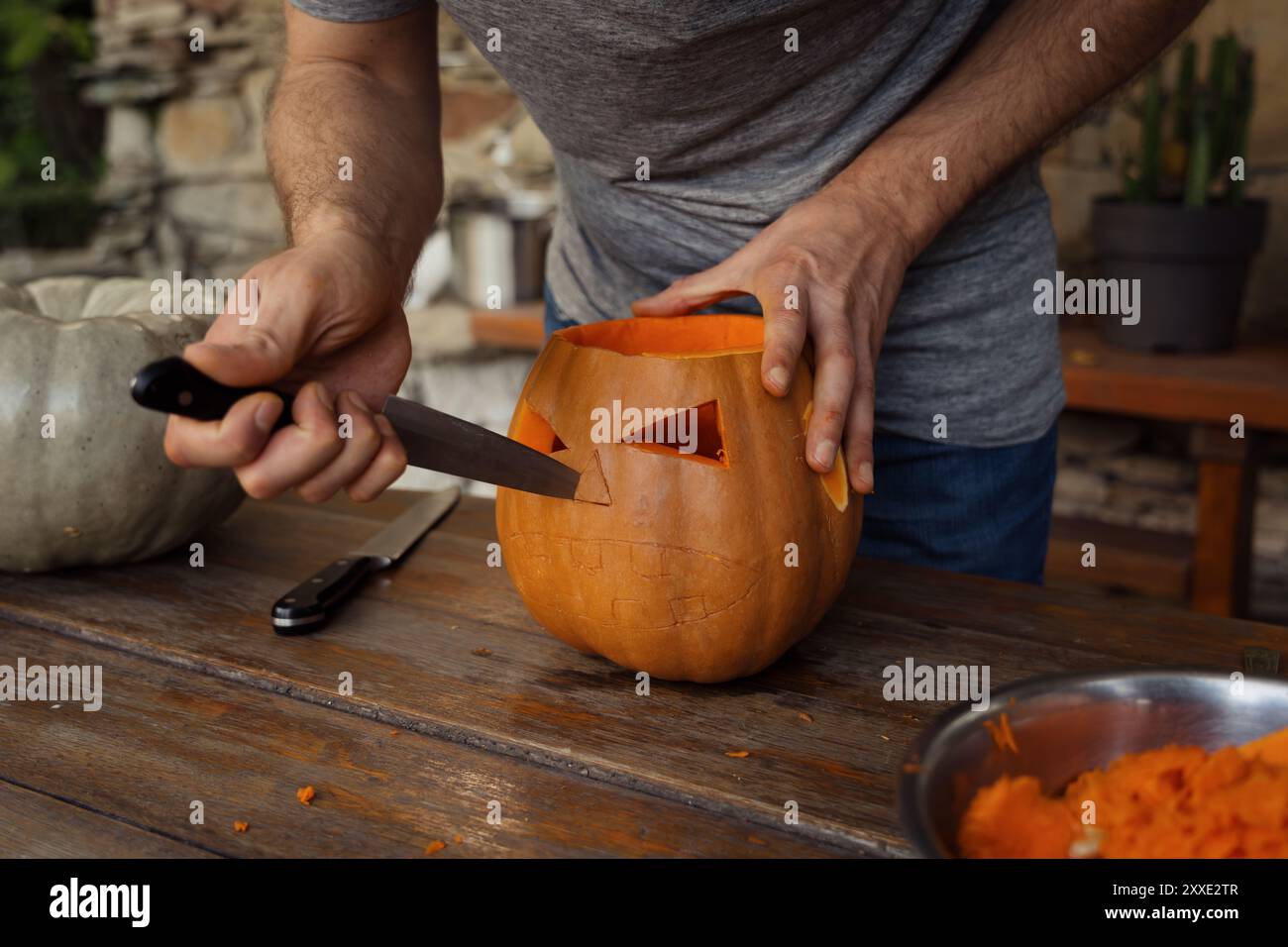 Hand schnitzt einen Kürbis zur Halloween-Dekoration auf einem Holztisch Stockfoto