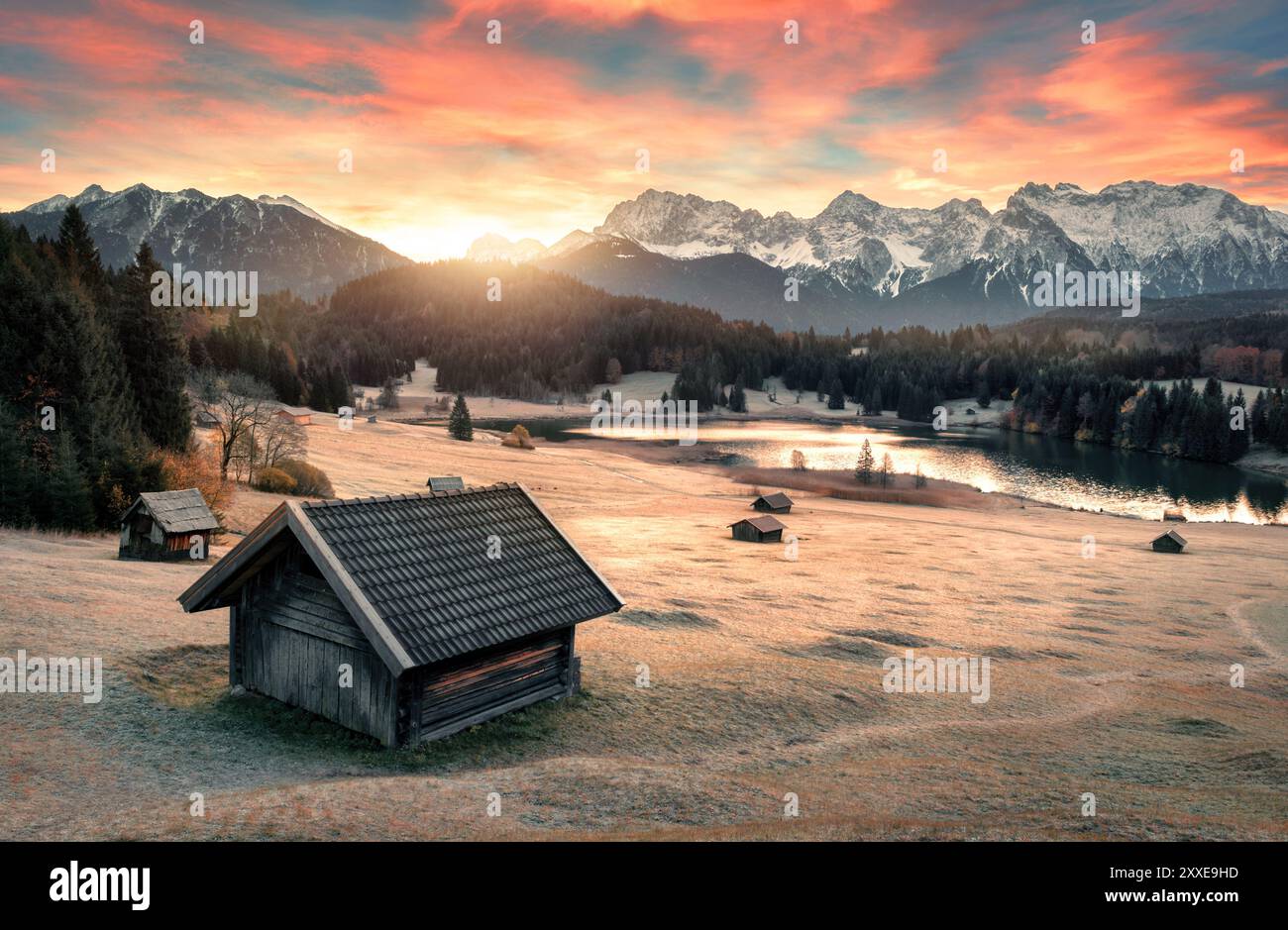 Sonnenaufgangslandschaft an einem See, mit einer Hütte im Vordergrund und Bergen im Hintergrund, gefrorener Wiese und bunten Wolken am Himmel Stockfoto