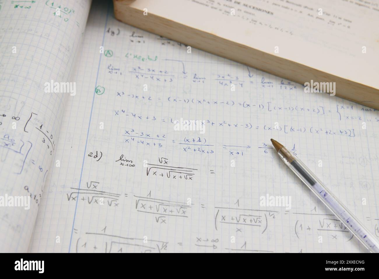 Abbildung eines Notizbuchs mit erweiterten mathematischen Hausaufgaben (Grenzen) neben einem Stift und einem Schülerbuch Stockfoto