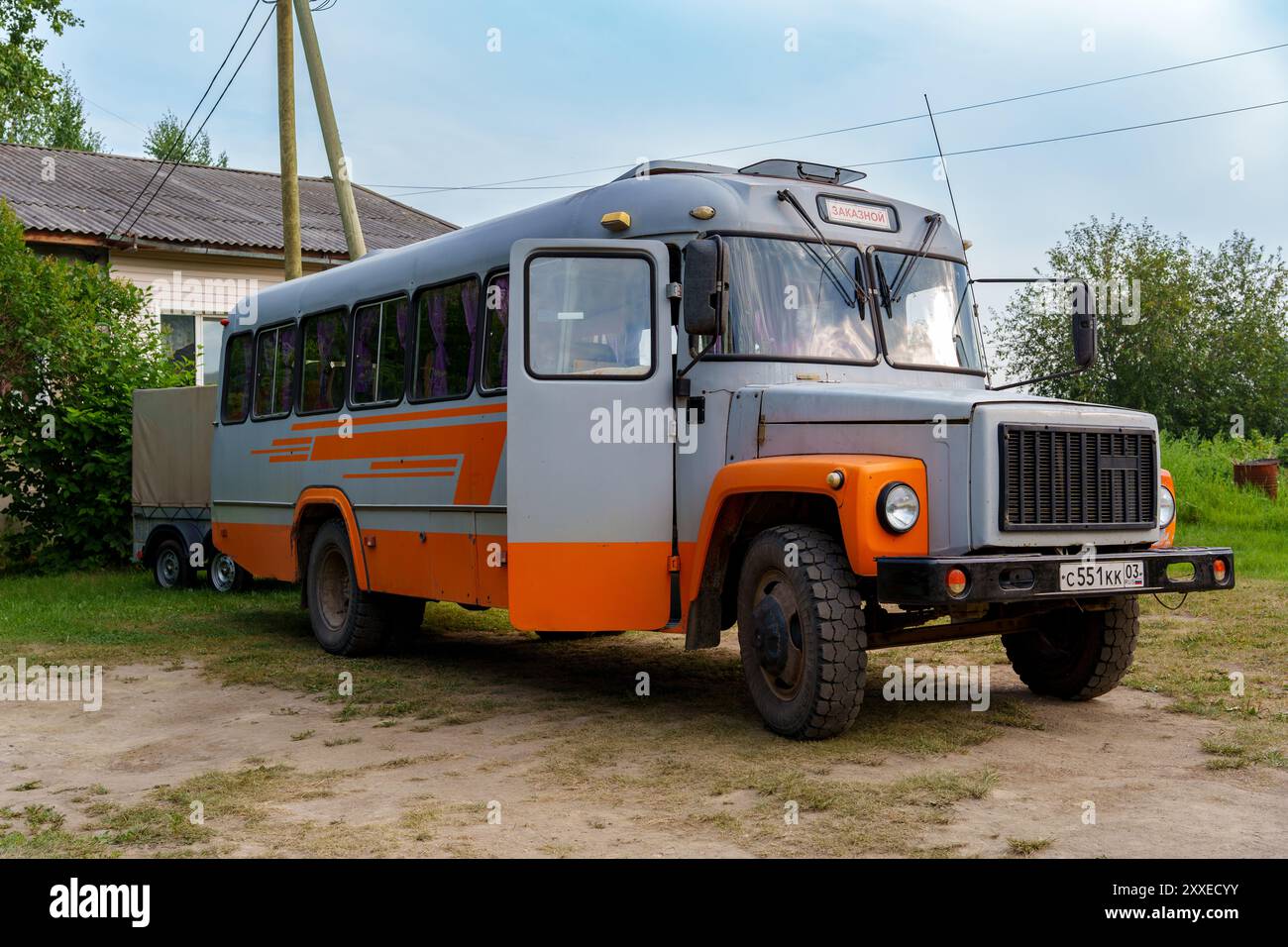 Ein Vintage-Bus aus sowjetischer Zeit mit orangefarbener und grauer Farbe, der in einer ländlichen Gegend in der Nähe eines Hauses geparkt ist und ein Gefühl von Nostalgie und historischem Transport weckt. Stockfoto