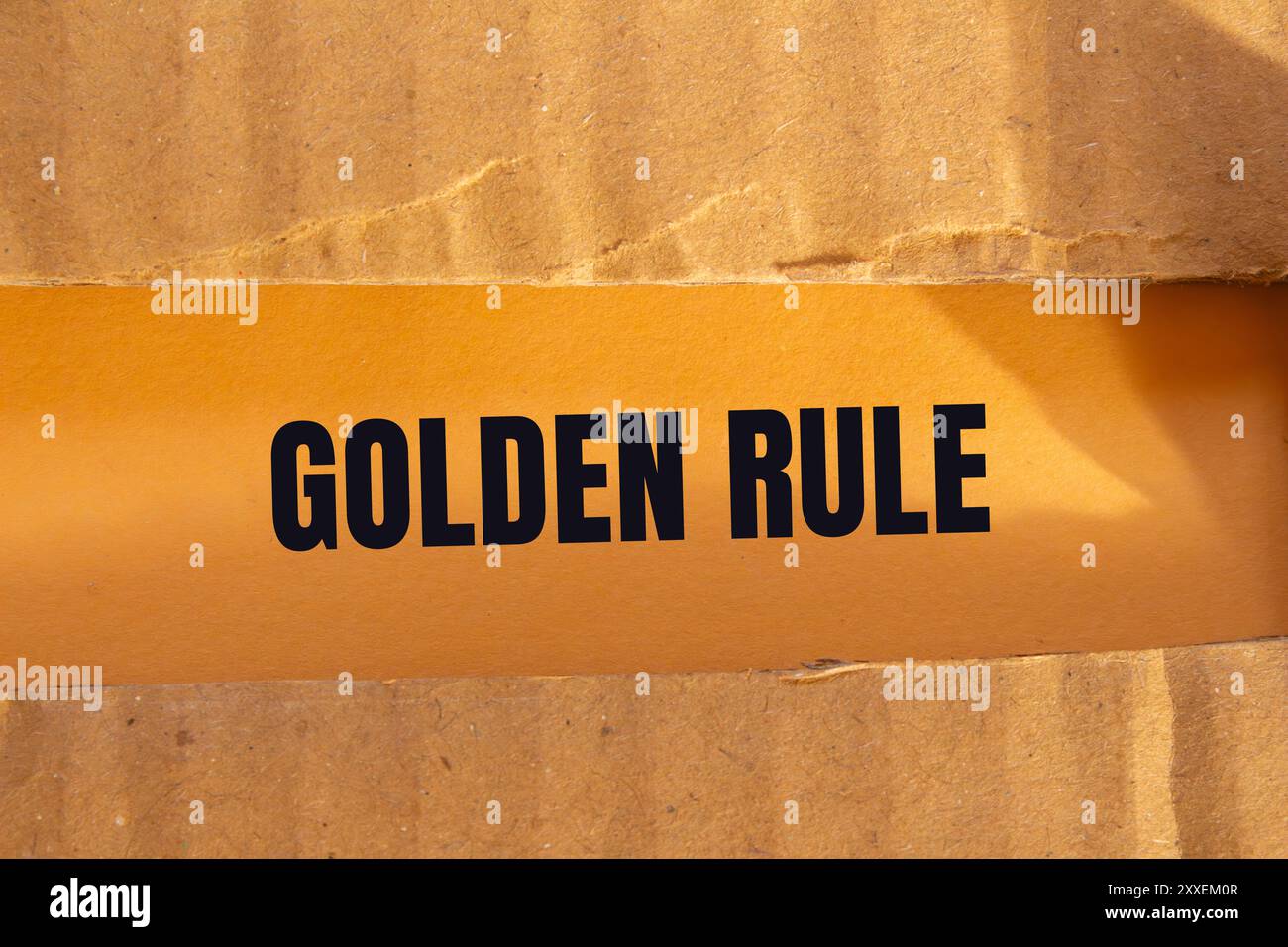 Goldene Regelnachricht auf zerrissenem Papppapier mit orangem Hintergrund. Konzeptionelles goldenes Regelsymbol. Kopierbereich. Stockfoto
