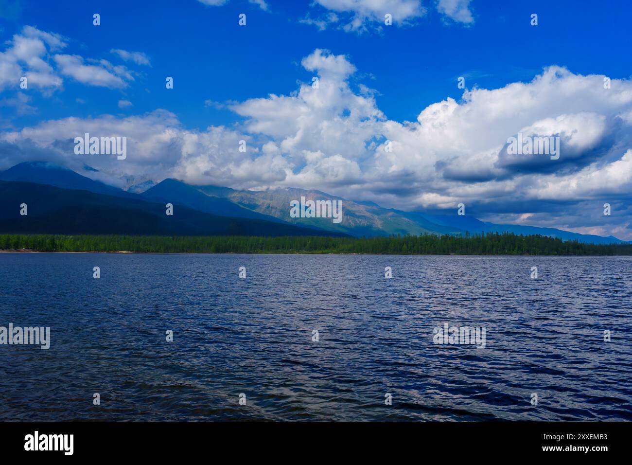 Ein ruhiger See mit glattem Wasser reflektiert das sanfte Licht eines nebeligen morgens, eingerahmt von fernen Bergen und einem von Bäumen gesäumten Ufer, was ein ruhiges A schafft Stockfoto